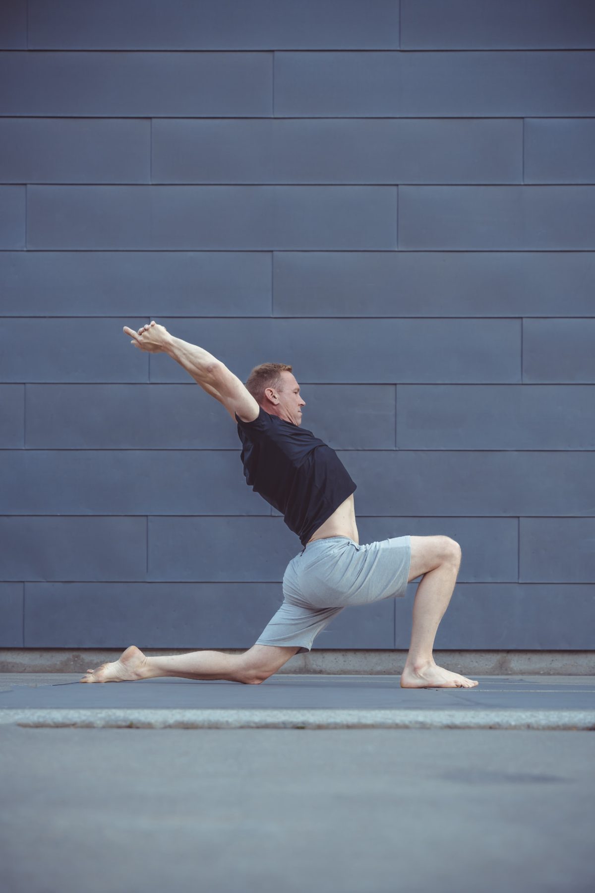 Christopher Gillett in a low lunge with arms overhead against a grey wall