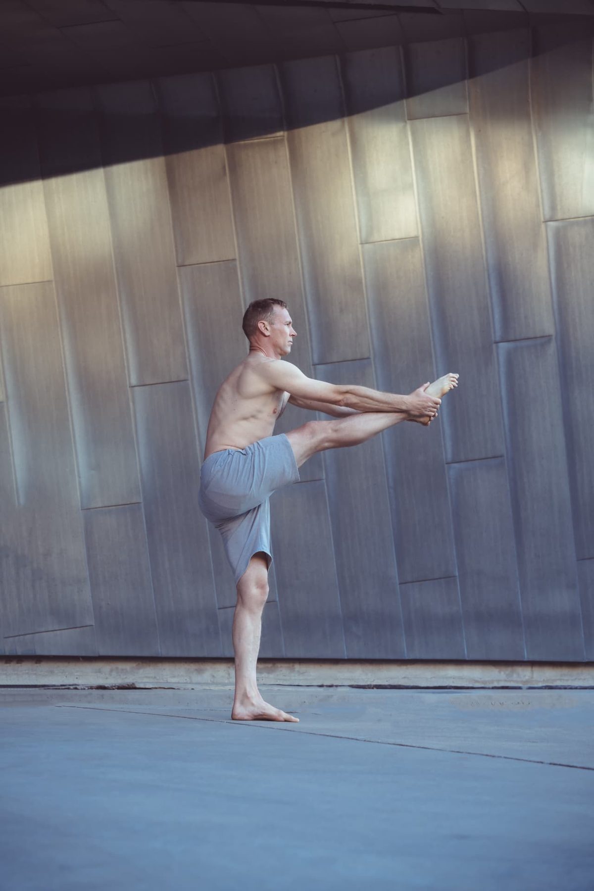 Christopher Gillett balancing in extended hand-to-big-toe pose against a metal wall
