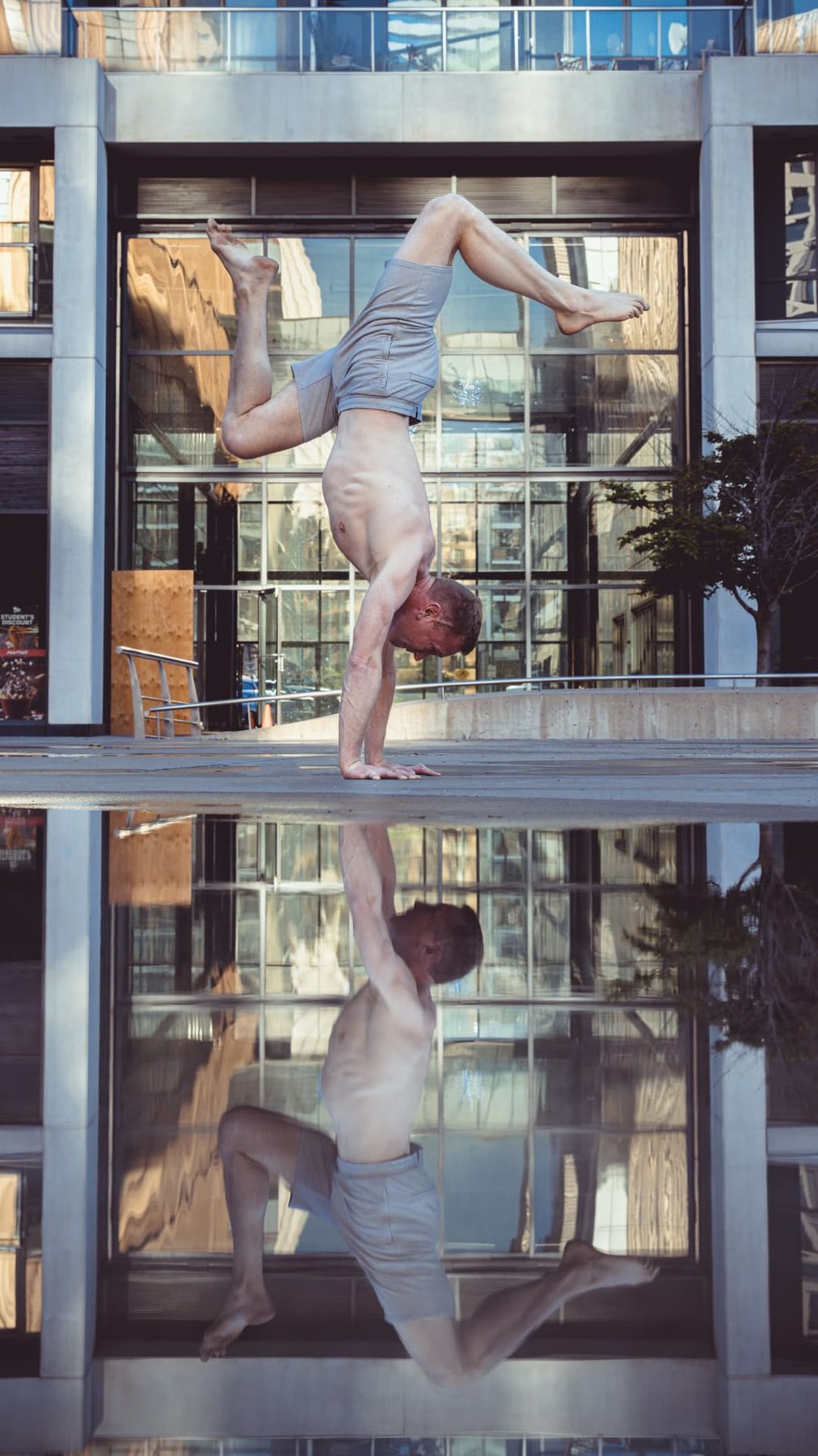 Christopher Gillett in a stag handstand mirrored in water